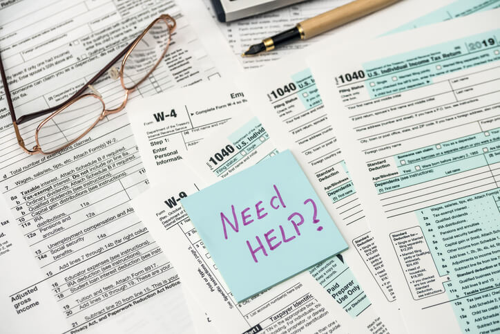 Scattered tax documents with a sticky note that reads 'Need Help?'
