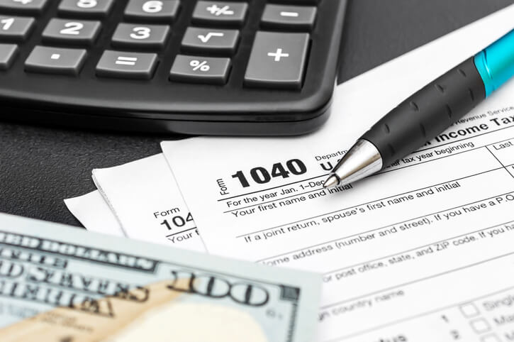 1040 Tax document with a hundred dollar bill, calculator, and a pen