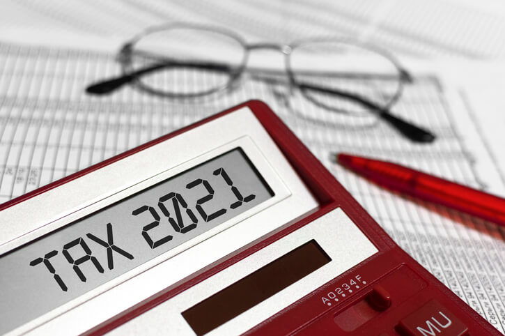 A calculator that displays Tax 2021 on it on top of spreadsheets with glasses in the background