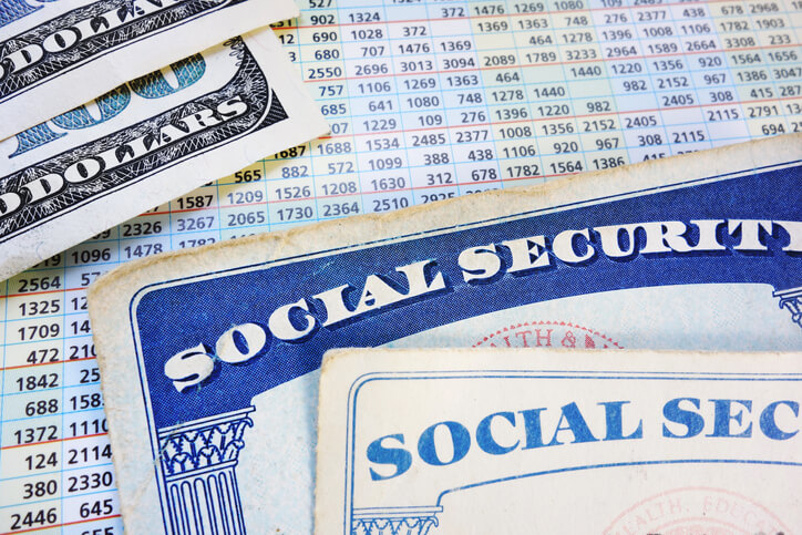 Social security cards and hundred dollar bills laying on top of a spreadsheet