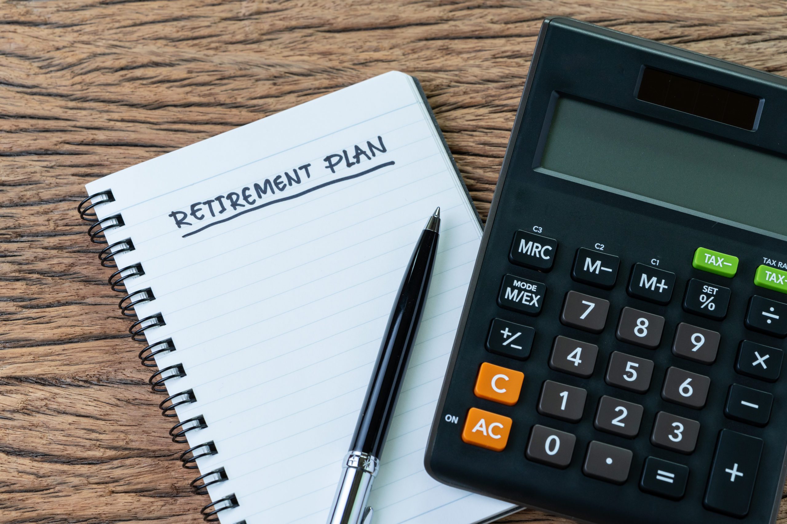 Retirement planning concept, calculator with empty notepad with pen and handwriting underline headline as Retirement Plan on wood table, plan of saving and investment for expense after retire life